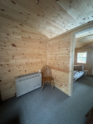 Une piĂšce aux murs en bois, avec un radiateur, une chaise et un lit prĂšs dâune fenĂȘtre.