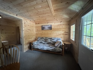 LâintĂ©rieur dâune cabane en bois, avec un lit, une chaise et une fenĂȘtre.