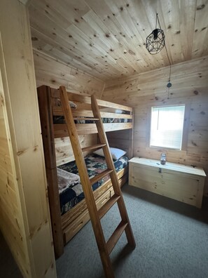 En køjeseng med en trætrap, et skrivebord med en lampe og et vindue med skodder.