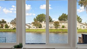 Blick durch große Fenster auf eine Wohngegend mit Häusern, ein Gewässer und eine Wiese.