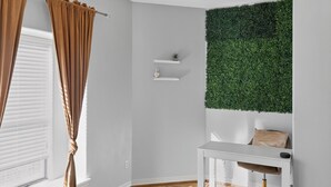 Una habitación con pared blanca, un tapiz verde, una consola blanca y una ventana con persianas.