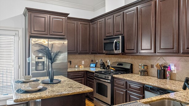 Una cocina moderna con armarios de madera oscura, encimeras de granito, electrodomésticos de acero inoxidable y horno empotrado.