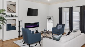 Una sala moderna con un televisor de pantalla plana, un ventilador de techo y un amplio ventanal con cortinas.