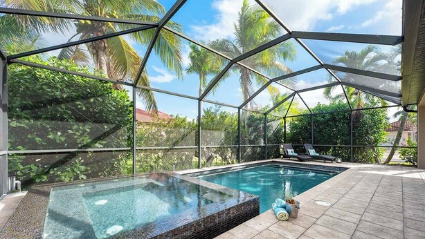 Une piscine à débordement entièrement vitrée, bordée de carreaux, entourée de chaises longues et offrant une vue sur un jardin tropical.