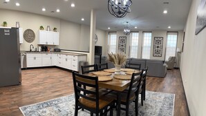 Cozinha ampla com armários brancos, uma ilha central e uma área de jantar com mesa e cadeiras de madeira.