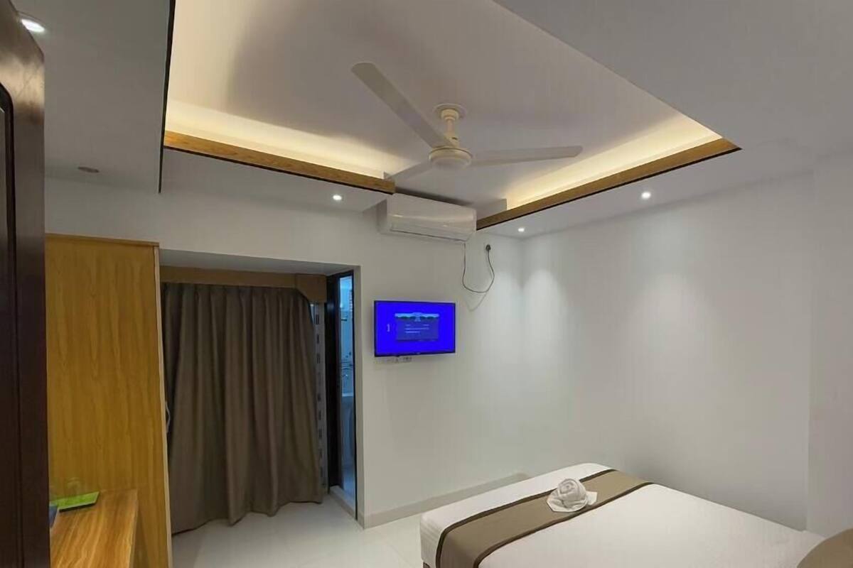 A modern hotel room with a bed, a ceiling fan, a flat-screen TV mounted on the wall, and a door leading to another room.
