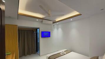 A modern hotel room with a bed, a ceiling fan, a flat-screen TV mounted on the wall, and a door leading to another room.