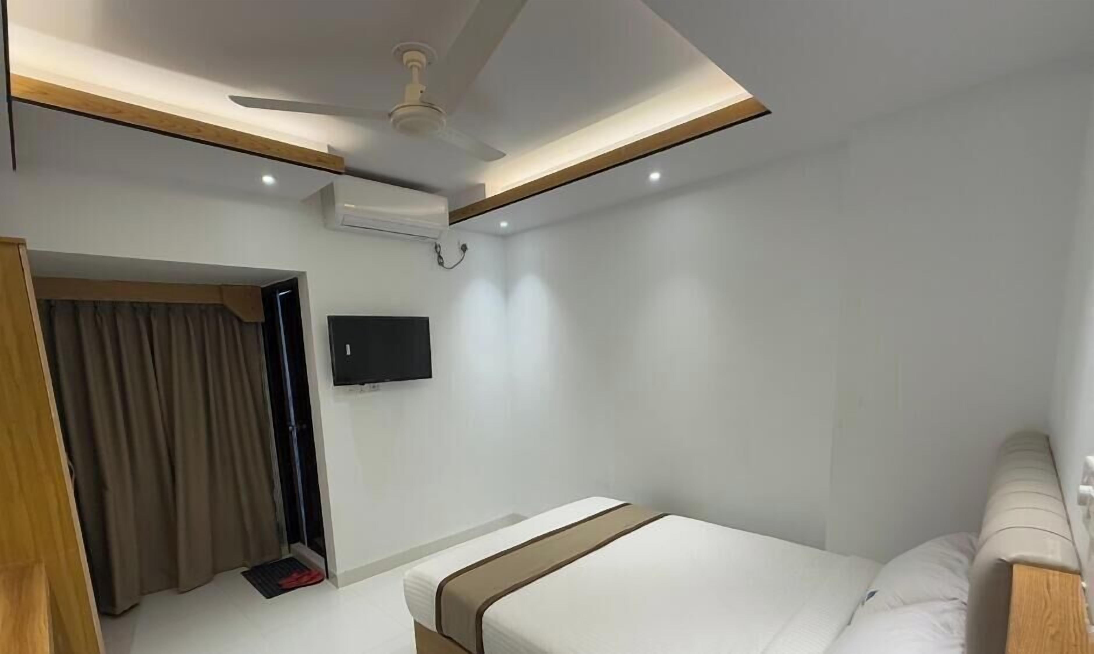 A modern hotel room with a bed, a ceiling fan, a TV, and a door leading to a bathroom.