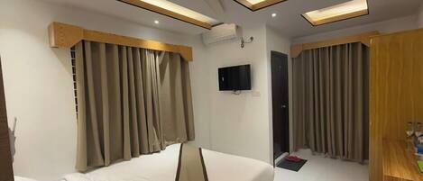 Una habitación de hotel con cama, cortinas, televisor y ventilador de techo.