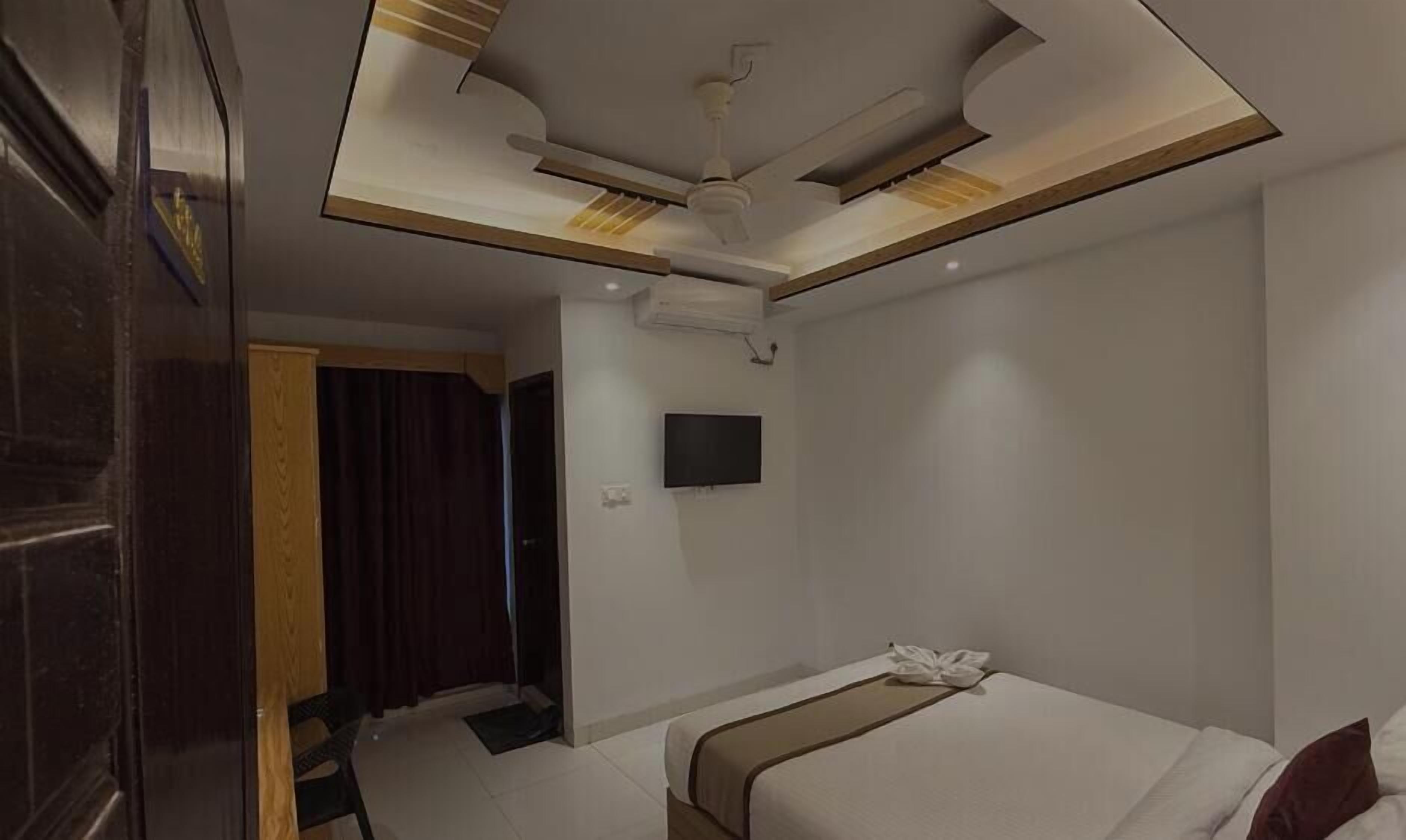 A modern hotel room with a bed, a flat-screen TV, and a ceiling with recessed lighting.