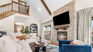 A spacious living room with a stone fireplace, a large flat-screen TV, a blue sofa, and a white sectional sofa. - *New* Sawyer's Rest - Hot Tub+ (Hollister)