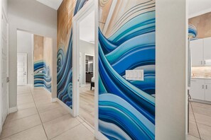 A hallway with a modern design, featuring a wavy blue and teal wall mural, a wooden accent wall, and a kitchen area with white cabinets. - Bliss at Reunion-TT489 (Kissimmee)