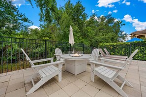 A patio with a round table and four Adirondack chairs, surrounded by a black metal fence, with trees and a building in the background. - Desert Waves at Reunion-TT489 (Kissimmee)