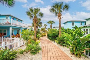 A pathway flanked by lush greenery and two blue buildings with white railings. - VW26 Friday Life, Shared Heated Pool, Pet Friendly, Gated Community (Port Aransas)
