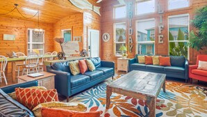 L’intérieur d’un chalet confortable, avec un canapé bleu, une table basse en bois et un coin repas comprenant des chaises blanches et une table en bois.