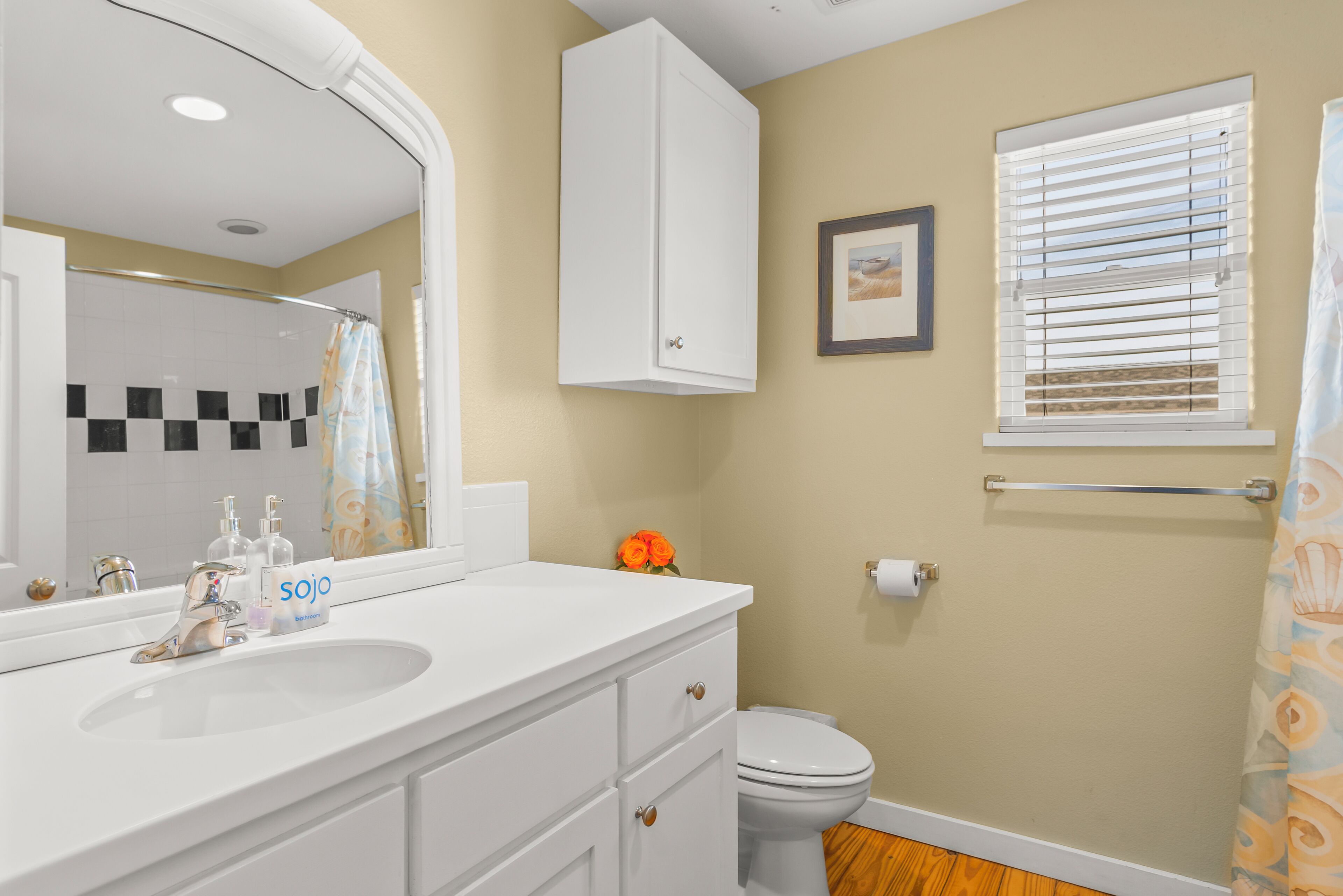 A bathroom with a white vanity, a large mirror, a toilet, and a window with blinds.