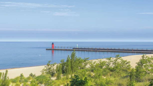 A coastal scene with a lighthouse and pier extending into calm waters, surrounded by greenery and a clear sky. - Deercreek Retreat in South Haven, Spacious 4BR perfect for family getaways! (South Haven)