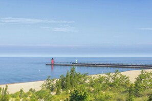 Eine Küstenansicht mit einem Leuchtturm und einer Steg, der sich in ruhiges Wasser erstreckt, umgeben von Grünpflanzen und einem klaren Himmel.