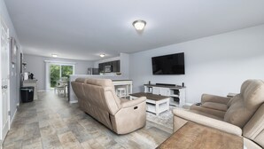 A modern living room with a beige sofa, a coffee table, and a flat-screen TV mounted on the wall. - Deercreek Retreat in South Haven, Spacious 4BR perfect for family getaways! (South Haven)