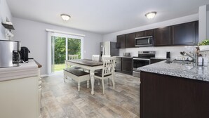 A modern kitchen with dark cabinets, a granite countertop, and a dining area with a table and chairs. - Deercreek Retreat in South Haven, Spacious 4BR perfect for family getaways! (South Haven)