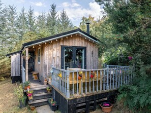 Una cabaña de madera con terraza, rodeada de un bosque denso.