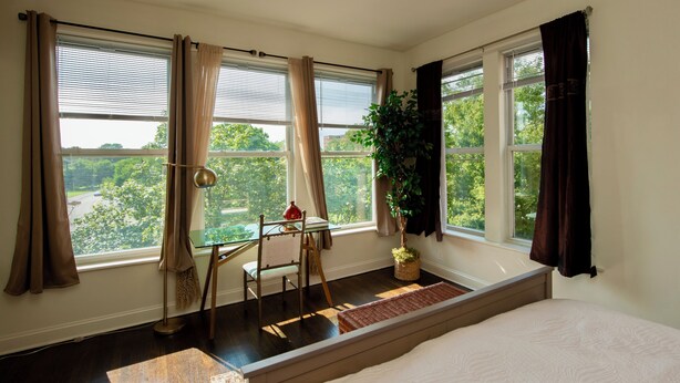 Un dormitorio con una cama grande, un escritorio con silla, una ventana con cortinas y una planta en maceta.