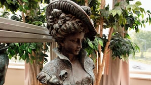 Una estatua de una mujer con un sombrero y vestido detallados, colocada en una maceta.