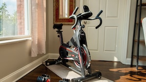 Una bicicleta estática con una colchoneta y mancuernas en una habitación con ventana y puerta.