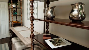 Una mesa de madera con un mantel tejido, una jarra de plata y un libro pequeño en una estantería.