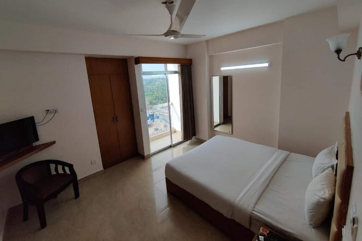 Ein Hotelzimmer mit Bett, Schreibtisch mit Stuhl, Deckenventilator, großem Fenster und Blick ins Freie.