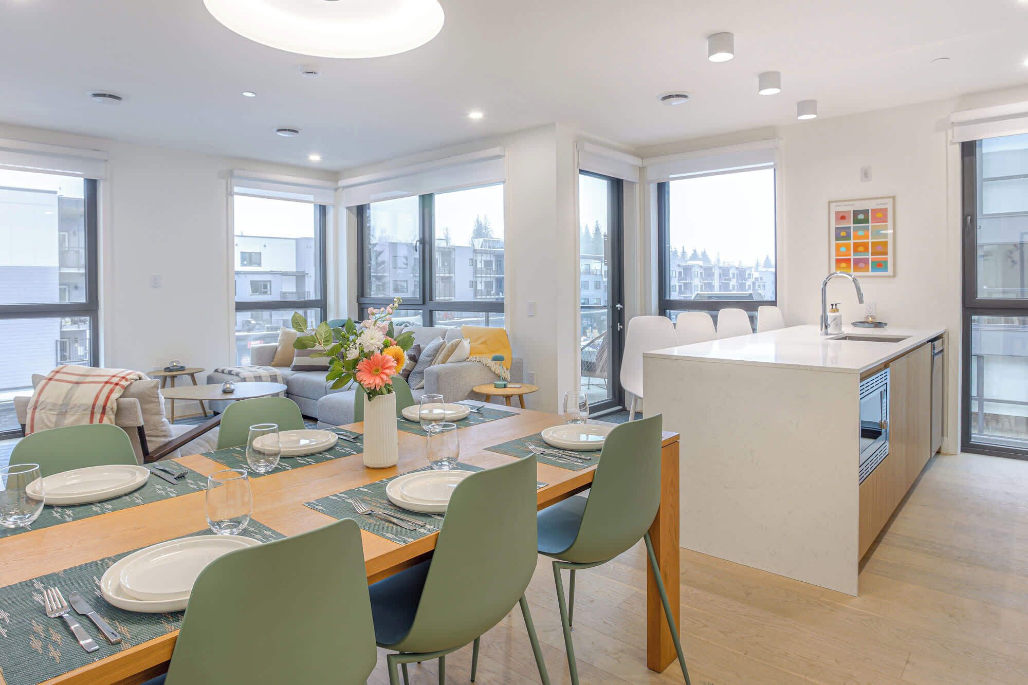 A modern apartment with a dining area, kitchen, and large windows offering city views.