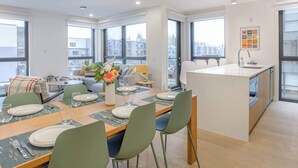 A modern apartment with a dining area, kitchen, and large windows offering city views. - Cedar Vista - condo with stunning mountain views (Revelstoke)