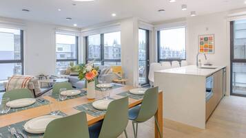 A modern apartment with a dining area, kitchen, and large windows offering city views.