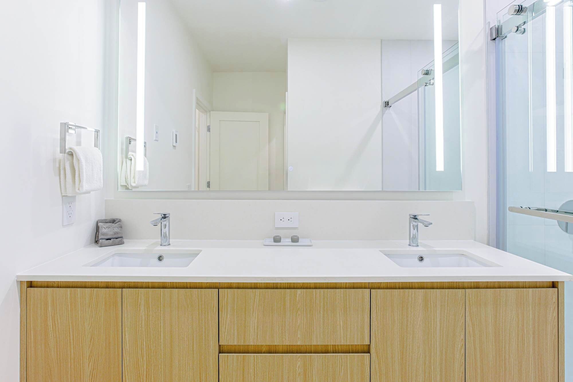 Un baño moderno con dos lavamanos, un espejo grande y una zona de ducha.