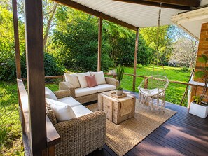 Un espacio de estar al aire libre cubierto con muebles de mimbre, una silla colgante y vistas a un jardín exuberante.