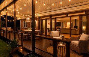 Une terrasse extérieure dotée de meubles en bois, de guirlandes lumineuses et d’une porte vitrée donnant sur un espace de vie intérieur.