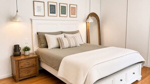 Une chambre à coucher bien rangée, avec un lit, des tables de chevet, une commode, un miroir et, au mur, des citations inspirantes encadrées.