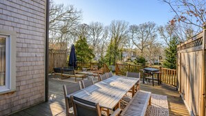 A wooden deck with outdoor furniture, including a table and chairs, and a grill. - Cozy Cape Retreat with Fenced Yard & Fire Pit (Harwich)