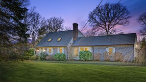 A two-story house with a sloped roof, dormer windows, and a chimney. - Cozy Cape Retreat with Fenced Yard & Fire Pit (Harwich)