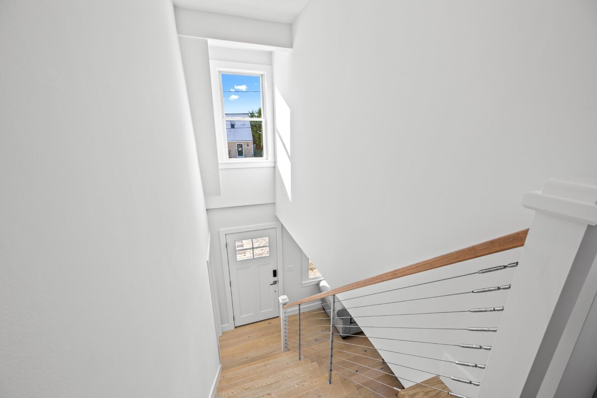 Una escalera moderna con barandilla de madera y balaustradas de metal, que conduce a una puerta blanca con un ventanal encima.