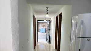 A hallway with a tiled floor, a white refrigerator, and a door leading to an outdoor area.