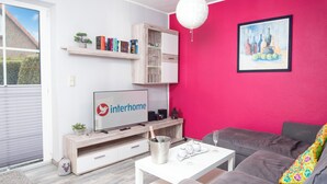 Una sala moderna con un televisor de pantalla plana, una estantería, una mesa de centro y un sofá gris.