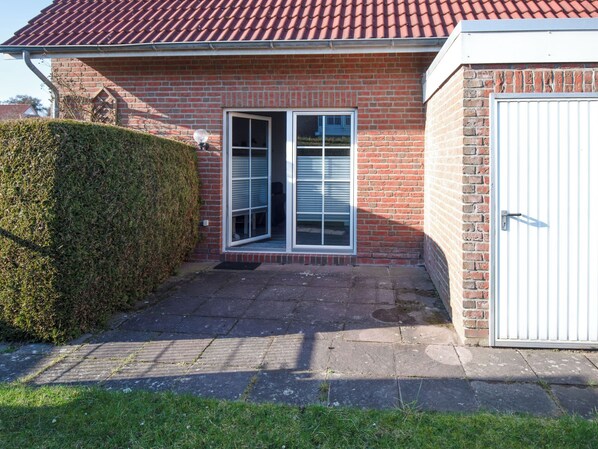 Een bakstenen huis met een rode pannendak, een witte garage deur en een kleine veranda met treden die leiden naar een deur met een raam.