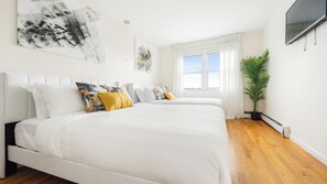 A modern bedroom with a large bed, a potted plant, and a window with curtains. - Luxury 3BR NY Home with Free Parking (White Plains)