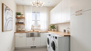 Une cuisine moderne avec des meubles blancs, un évier en acier inoxydable, un lave-linge encastré et un luminaire suspendu.