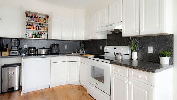 A modern kitchen with white cabinets, a granite countertop, a built-in oven, and a variety of appliances including a coffee maker and a blender. - Luxury 3BR NY Home with Free Parking (White Plains)