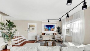 Un salon moderne avec un canapé, une table basse et un téléviseur. Un escalier mène à une autre pièce.