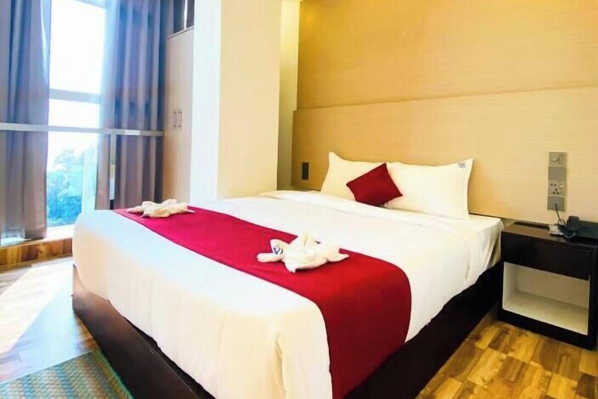 Une chambre d’hôtel avec un grand lit, une table de chevet, une commode et une fenêtre avec des rideaux.