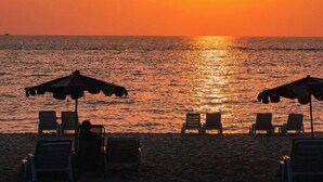 Ein Strand mit sonnigem Wasser, einem Fallschirm und Liegestühlen.