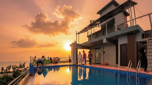 Ein Schwimmbecken mit Sonnenuntergangsblick, ein überdachter Bereich und ein Gebäude mit Balkon.